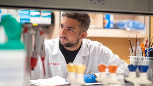 A researcher in a white coat works at a lab bench