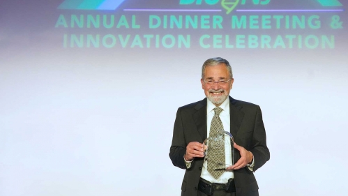 Chancellor Strom holds a plaque on a stage after receiving the BioNJ award
