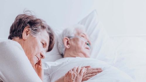 A woman sits by the bedside of an elderly man