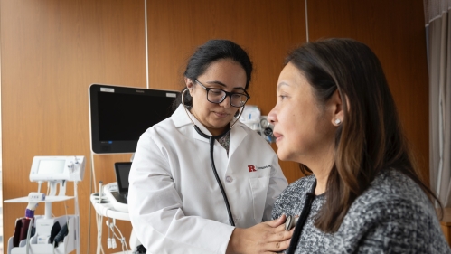 A Rutgers Health doctor listens to the heart of a clinical trial participant in an exam room