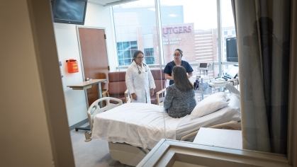 Looking through a glass window, health care providers are seen talking with a patient in a hospital room
