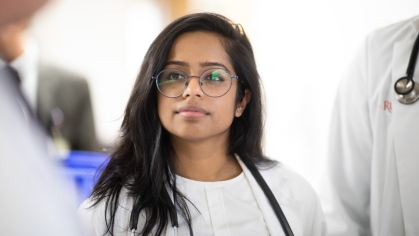 A medical student in a lab coat listens to an instructor