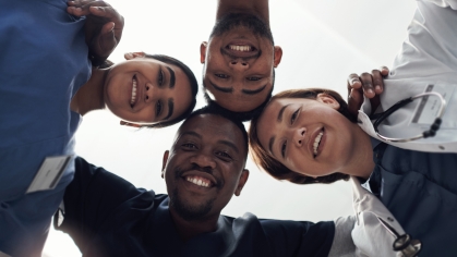 Four health care workers in a circle looking down at the camera 