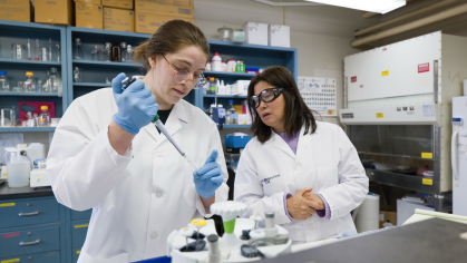 A professor watches as a pharmacy student practices lab skills 