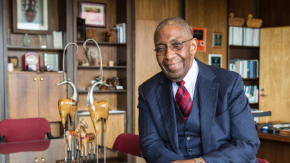 Dean Robert L. Johnson leans on a desk in his office. 