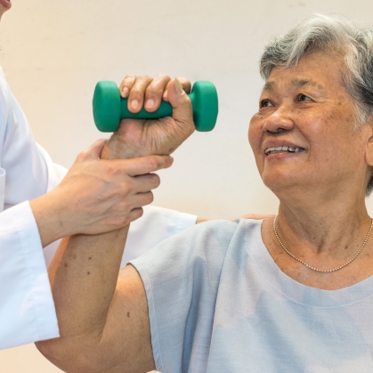 An elderly person holds a hand weight while a physical therapist assists