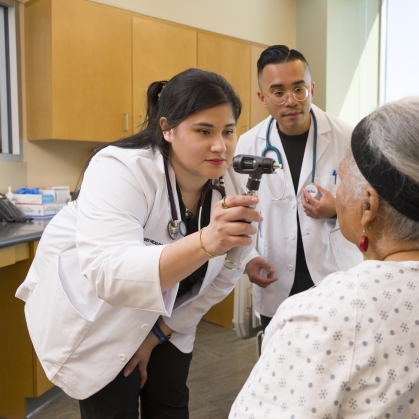 Nursing students examine a patient in a hospital room.