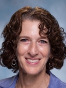 Janet Alder has chin-length brown curly hair and is wearing a purple shirt