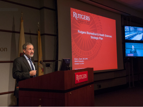 A person speaking at a podium showing a presentation with a red background