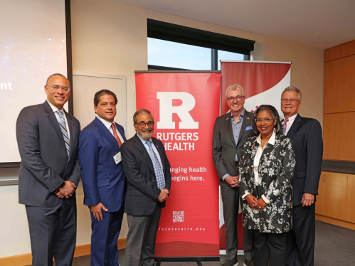 A group of Rutgers leaders standing in front of a Rutgers Health banner
